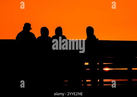 Isle Of Palms, Usa. Dezember 2024. Eine Gruppe von Menschen beobachtet den Sonnenaufgang an einem kalten Morgen zur Wintersonnenwende vom Isle of Palms Pier, 21. Dezember 2024 in Isle of Palms, South Carolina. Die Wintersonnenwende ist der kürzeste Tag der nördlichen Hemisphäre und markiert den Beginn des Winters. Quelle: Richard Ellis/Richard Ellis/Alamy Live News Stockfoto