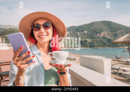 Junge Frau, die Handy benutzt und Kaffee in einer Bar am Meer trinkt Stockfoto