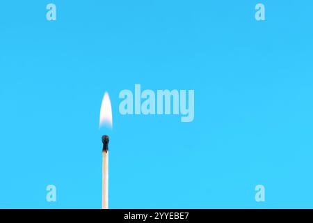 Hölzerner Streichholzstab mit brennender Flamme auf klassischem blauem Hintergrund in einem Studio. Feuer- und Minimalismus-Konzept mit Kopierraum für Text oder Design Stockfoto