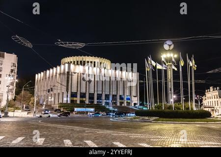 Ein großes Gebäude mit einem Uhrenturm und Fahnen oben. Das Gebäude ist nachts beleuchtet Stockfoto