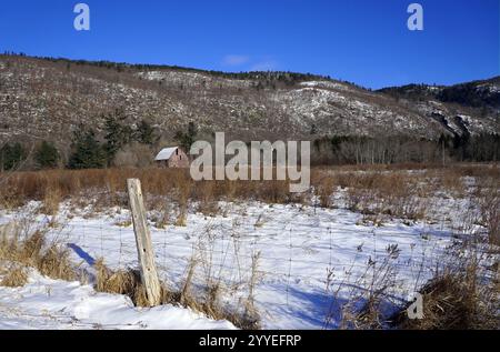 Verwitterte Scheune am Fuße eines Hügels mit einem schneebedeckten Feld und Zaunpfosten im Vordergrund Stockfoto