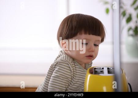 Kleiner Junge, der mit Toaster in der Küche spielt. Gefährliche Situation Stockfoto