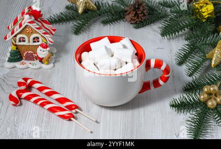 Festliche Tasse mit Lutscher-Griff mit Kaffee und Marshmallows auf Holztisch in gemütlicher Atmosphäre Stockfoto