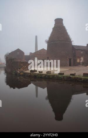 Ein alter Flaschenofen in Stoke auf Trent spiegelt sich im Kanal wider. An einem nebeligen Tag, um eine Atmosphäre zu schaffen, reflektiert es sich im Kanal Stockfoto