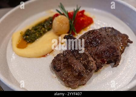 Saftiges gegrilltes Rindfleisch, serviert mit cremigem Kartoffelpüree, gerösteten Tomaten und garniert mit Kräutern. Stockfoto
