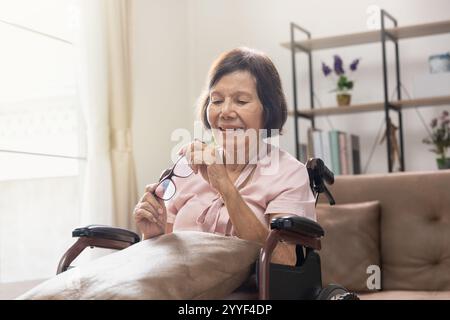 Ältere Frau mit Brille, die zu Hause auf dem Rollstuhl sitzt Stockfoto