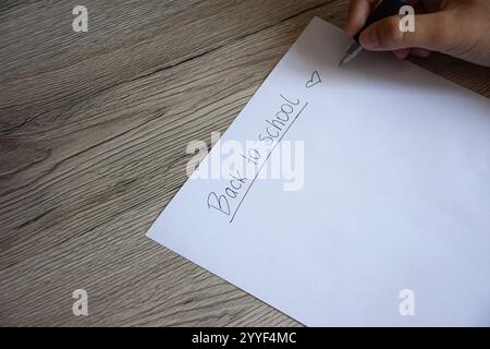 Der Satz „Back to School“ ist in schwarzer Tinte in der oberen linken Ecke des Papiers handgeschrieben, begleitet von einem kleinen Herz daneben. Stockfoto