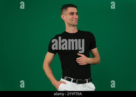 Hübscher junger Mann auf grauem Hintergrund, der in die Kamera schaut. Porträt eines lachenden jungen Mannes mit Händen in Taschen, die an eine graue Wand geneigt sind. Ein glücklicher Kerl lächelt. Hochwertige Fotos Stockfoto