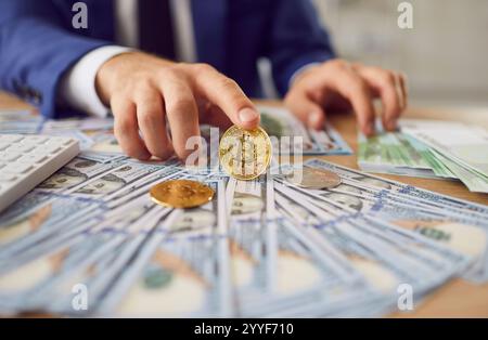 Erfolgreicher Aktienhändler, der am des sitzt, mit Geld-Dollar-Bargeld, der Bitcoin in Händen hält. Stockfoto