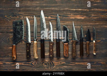 Verschiedene Küchenmesser sind ordentlich auf einem rustikalen Holztisch angeordnet und zeigen verschiedene Formen und Größen, einschließlich Trennmesser, Universalmesser und che Stockfoto
