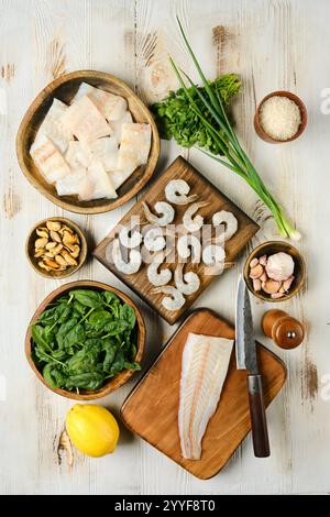 Auf der Küchenarbeitsplatte finden Sie eine Auswahl an frischen Meeresfrüchten und lebendigem Gemüse, darunter Garnelen, Fischfilets und Blattgemüse Stockfoto