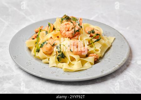Ein lebhaftes Gericht mit Fettuccine-Pasta, garniert mit saftigen Garnelen und frischen Kräutern, sitzt elegant auf einem gemusterten Teller und präsentiert ein köstliches Cu Stockfoto