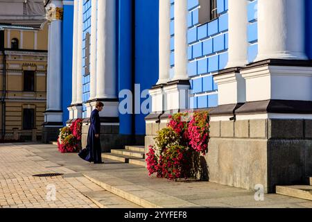 Eine Frau in langem Kleid geht an einem Gebäude mit einer blau-weißen Fassade vorbei. Das Gebäude hat ein großes Fenster auf der Vorderseite und einen Balkon mit Topf pla Stockfoto