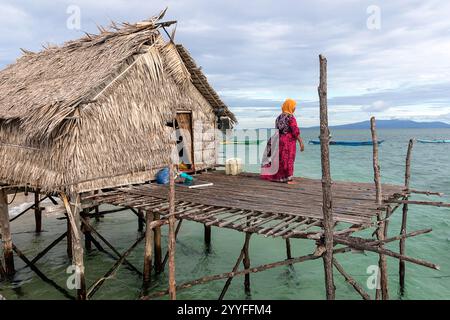 Frau aus Bajau laut Minderheit in traditioneller Kleidung auf einer Holzterrasse eines Hauses auf Stelzen mitten im Meer, Muna, Indonesien Stockfoto