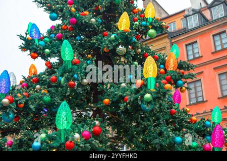 Geschmückter Weihnachtsbaum mit farbenfrohen Ornamenten für eine festliche Feiertagsatmosphäre. Hintergrund mit Gebäuden im europäischen Archit Stockfoto