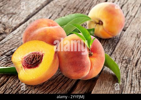 Reife rote saftige Pfirsiche mit grünem Blatt auf hölzernem Hintergrund. Stockfoto