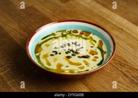 Eine warme Schüssel cremige Kürbissuppe, garniert mit einem Spritzer grüner und brauner Öle, garniert mit knusprigen Kürbiskernen. Die lebendige Präsentation fügt hinzu Stockfoto