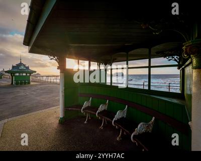 Traditionelle grüne Holzhütten an der North Promenade bei Blackpool mit Sonnenuntergang hinter dem North Pier in der Ferne. Stockfoto