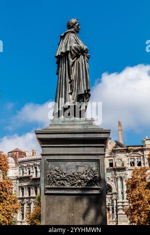 Eine Statue eines Mannes steht vor einem Gebäude. Die Statue besteht aus Bronze und ist sehr detailliert. Der Himmel ist blau und es gibt Wolken im B Stockfoto