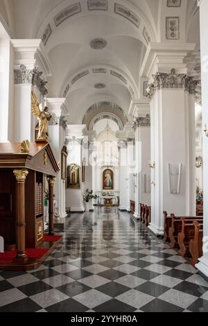 Ein langer, schmaler Raum mit weißen Säulen und einem Holzaltar. Der Raum ist voller Bänke und ein paar Statuen. Die Atmosphäre ist feierlich und friedlich Stockfoto