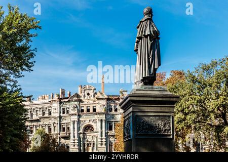 Eine Statue eines Mannes steht vor einem Gebäude mit viel Schaden. Der Himmel ist blau und es gibt Bäume im Hintergrund Stockfoto