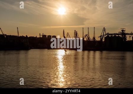 Das Bild fängt einen wunderschönen Sonnenuntergang über einem ruhigen Gewässer mit einem großen Kran im Hintergrund ein. Die Szene ist friedlich und ruhig, mit Stockfoto