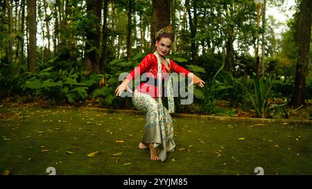 Eine traditionelle sundanische Tänzerin in einem roten Kostüm, das die Schönheit und den Reichtum der indonesischen Kultur widerspiegelt, während sie am Morgen im Wald ist Stockfoto