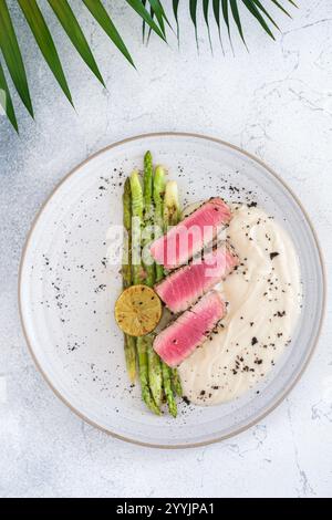 Ein Gourmet-Gericht von oben mit gebratenen Thunfischscheiben, gegrillter Limette, Spargel und cremigem Püree, elegant auf einer weißen Platte angeordnet Stockfoto