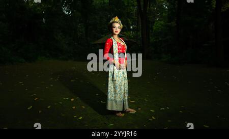 Eine traditionelle indonesische Tänzerin bezaubert mit ihrem wunderschönen Aussehen und trägt ein rotes Kostüm, das das Auge des Publikums im Wald i erregt Stockfoto