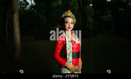 Eine traditionelle indonesische Tänzerin in rotem Kostüm, die tagsüber eine starke visuelle Anziehungskraft vor dem Publikum schafft Stockfoto