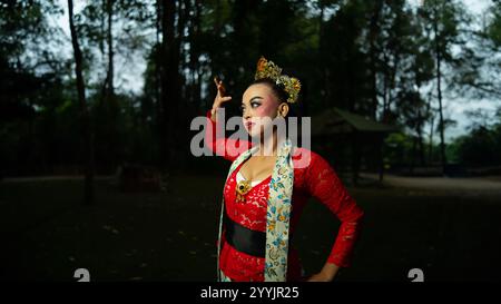 Eine traditionelle indonesische Tänzerin in rotem Kostüm, die tagsüber eine starke visuelle Anziehungskraft vor dem Publikum schafft Stockfoto