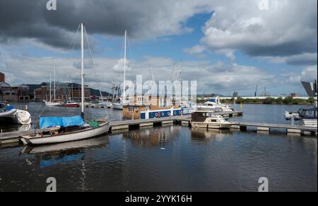 Boote und Yachten vertäuten an schwimmenden Docks am Fluss Lagan in Belfast, Nordirland, mit modernen Gebäuden und einem teilweise bewölkten Himmel im Hinterland Stockfoto