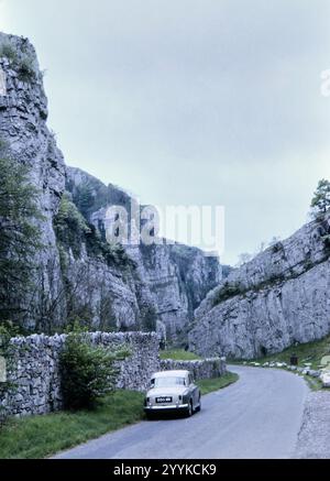 Historisches Foto eines alten Rover Autos, das am Rande einer Landstraße geparkt wurde, die zu Kalksteinklippen führt, Cliff Road, Cheddar Gorge, Mendip Hills, Somerset, England, Großbritannien in den 1960er Jahren Stockfoto