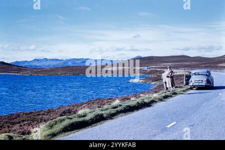 Historisches Foto von Menschen an einem See oder See und einem alten Rover Auto, das in den 1960er Jahren in Schottland in den schottischen Highlands geparkt wurde Stockfoto