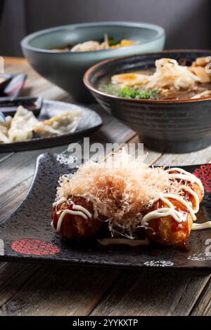 Blick auf einen Teller Takoyaki mit einer Vielzahl anderer japanischer Gerichte im Hintergrund. Stockfoto