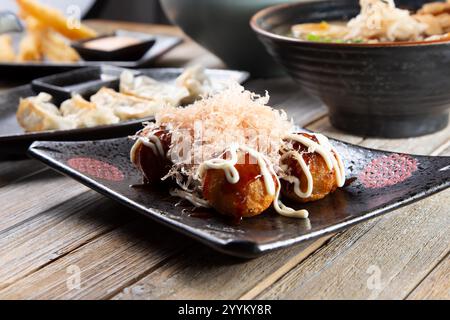 Ein Blick auf einen Teller Takoyaki und andere japanische Vorspeisen auf einem Tisch. Stockfoto
