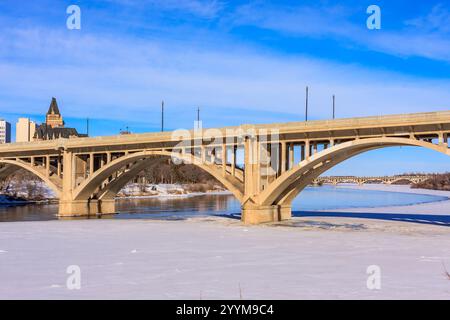 Eine Brücke überspannt einen Fluss mit einem verschneiten Ufer. Die Brücke ist eine große, bogenförmige Struktur mit einer grauen Farbe. Der Himmel ist klar und blau, und der Schnee auf dem gr Stockfoto