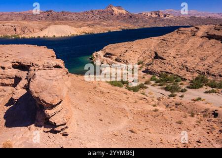 Eine felsige Wüstenlandschaft mit einem Gewässer in der Ferne. Das Wasser ist ruhig und klar, und der Himmel ist blau. Die Szene ist friedlich und ruhig Stockfoto