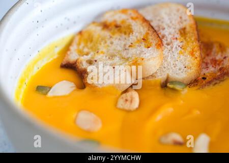 Eine lebendige Schüssel mit cremiger Kürbissuppe, garniert mit geröstetem Brot und bestreut mit Nüssen Stockfoto