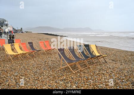 Lyme Regis Dorset UK Winterwochenende im Regen am Strand mit leeren Liegestühlen Stockfoto