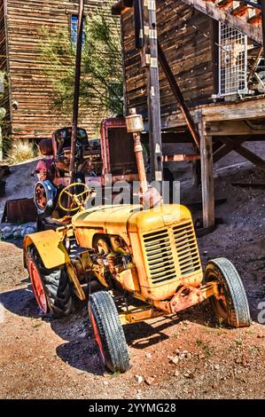 Ein alter gelber Traktor sitzt auf einem Feld. Der Traktor ist rostig und hat ein abgenutztes Aussehen. Nostalgiekonzept und Zeitverlauf Stockfoto