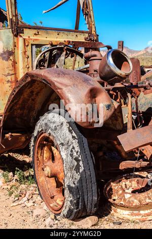 Ein alter, verrosteter Truck mit gebrochenem Vorderreifen. Der Reifen ist schwarz und hat viel Rost. Der Lkw steht auf einem Feld und der Himmel ist blau Stockfoto