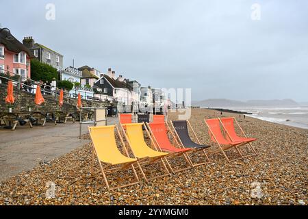 Lyme Regis Dorset UK Winterwochenende im Regen am Strand mit leeren Liegestühlen Stockfoto