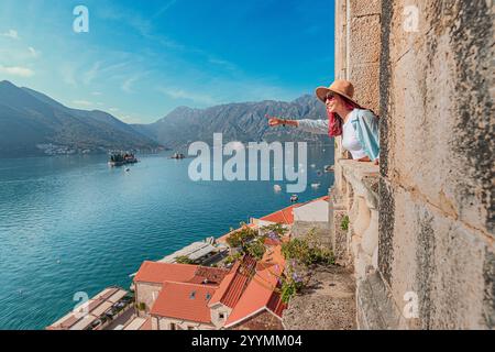 Frau, die von einem Kirchturm in Perast, Montenegro, auf die malerischen Inseln unserer Frau der Felsen und des Heiligen Georg zeigt Stockfoto