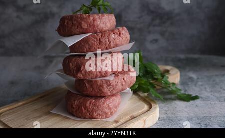 Ein Stapel Fritsch, bereit zum Kochen von Beefburger-Pasteten auf einem Holzbrett mit einer Beilage aus Kräutern. Stockfoto
