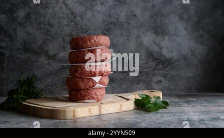 Ein Stapel Fritsch, bereit zum Kochen von Beefburger-Pasteten auf einem Holzbrett mit einer Beilage aus Kräutern. Stockfoto