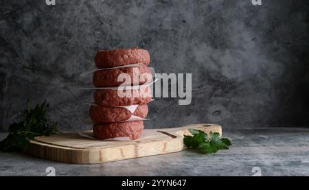Ein Stapel Fritsch, bereit zum Kochen von Beefburger-Pasteten auf einem Holzbrett mit einer Beilage aus Kräutern. Stockfoto