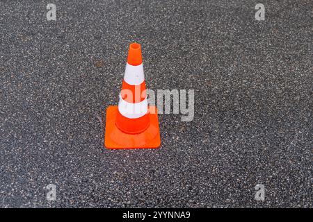 Gestreifte orangefarbene Kegel auf der Asphaltstraße. Orangefarbener Plastikkegel auf der Straße. Baukegel markieren einen Teil der Straße mit einer Schicht frischen Asphalts. Stockfoto