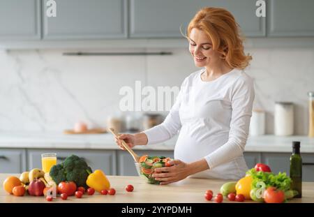 Schwangere Frau, die einen frischen Salat in einer modernen Küche zuhause zubereitet Stockfoto