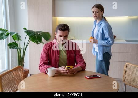 Die Frau las heimlich die Nachrichten des Ehemanns über die Schulter, während er in der Küche plauderte. Misstrauen, Vertrauensfragen Stockfoto